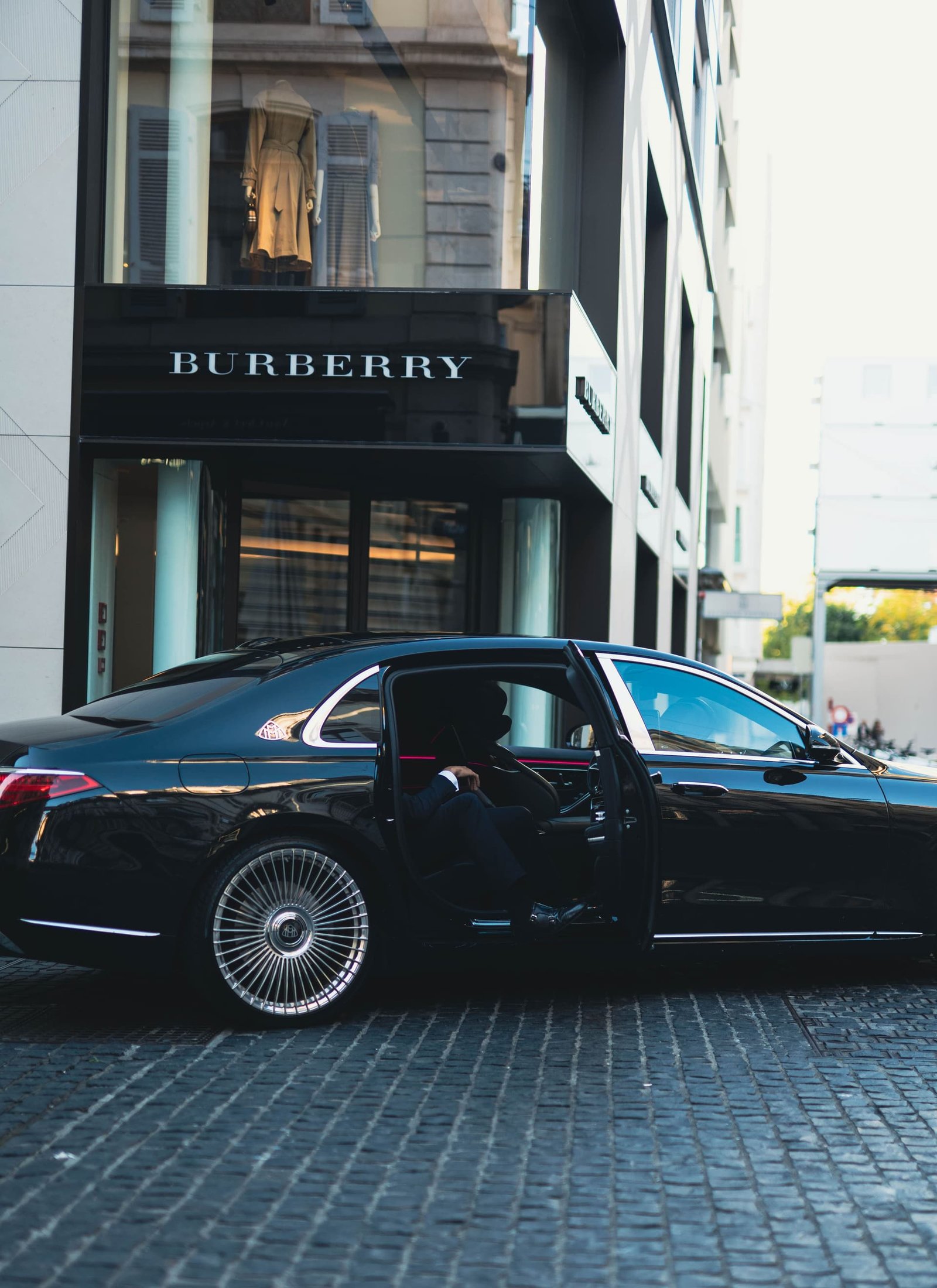 Chauffeur ouvrant la portière arrière d'une Mercedes-Maybach S 580 noire dans une rue pavée du centre-ville